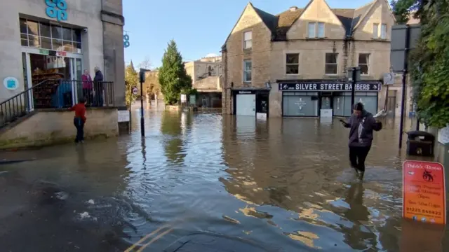 A person wearing dark clothing walks through the flood water