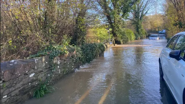 Cars trying to pass through Down Road in Winterbourne which is flooded