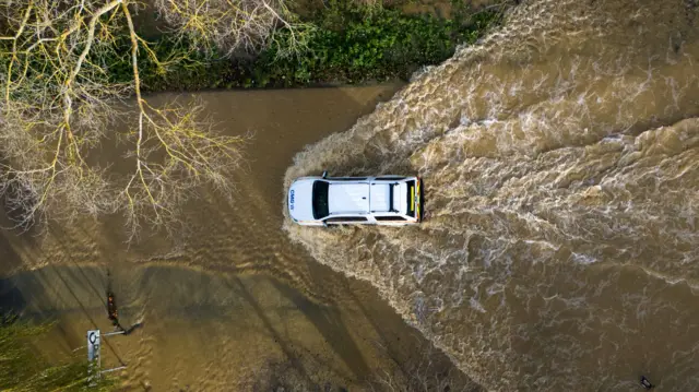 An aerial photo of a car driving through flood water