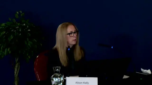 Alison Kelly, sat behind the witness desk, with long light brown hair and glasses