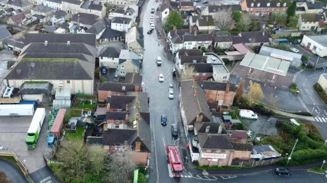 Flooded road seen from a drone, with cars trying to progress along it.