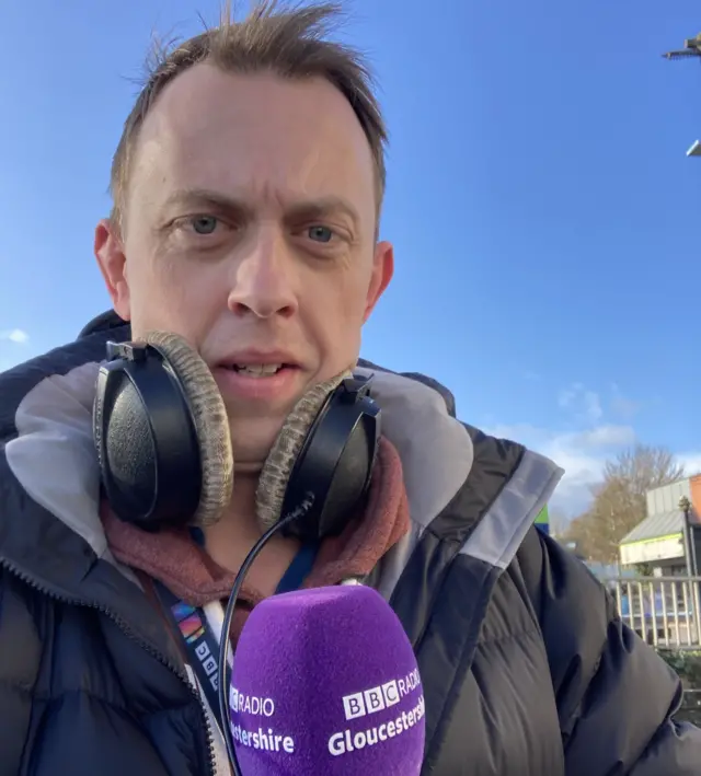 BBC reporter David Smith with headphones around his neck and a BBC Gloucestershire microphone