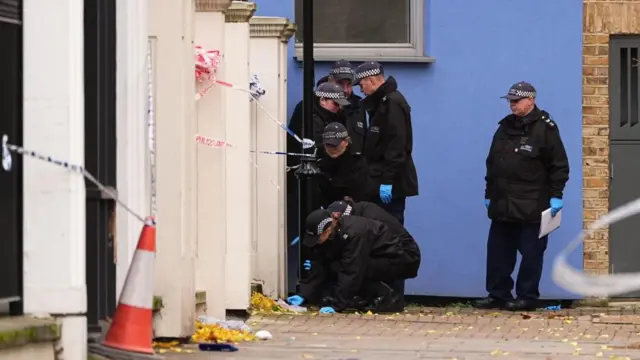 Two police officers crouch down by a footpath as others look on