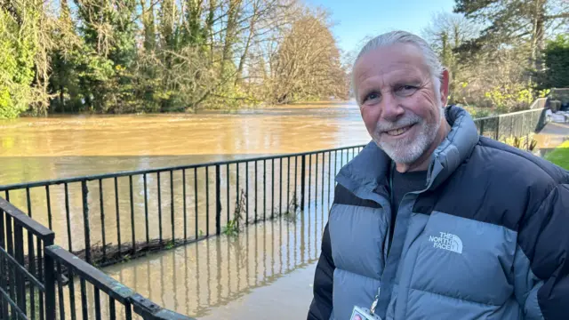 Councillor Ross Henning standing in front of flood water in Chippenham