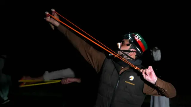 A protester uses a slingshot to throw a stone towards the police during the rally in Swabi