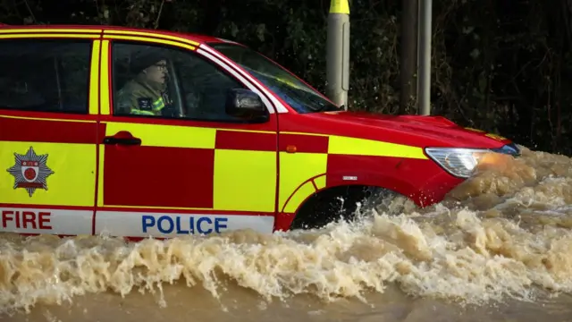 A fire and police car drives through flood water which nearly goes over the bonnent.