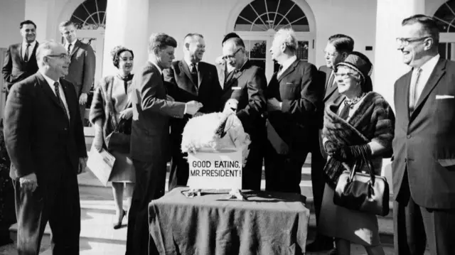 A black and white photo of John F Kennedy and other officials with a turkey in front of the White House