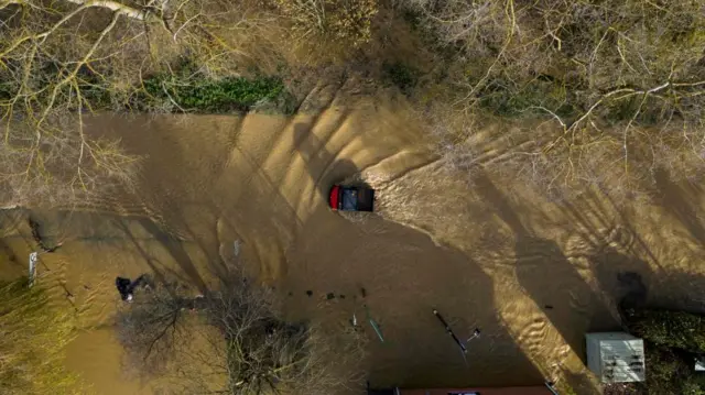 A vehicle drives through floodwater at the Billing Aquadrome in Northamptonshire.