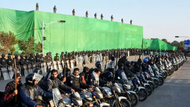 Police officers in Islamabad sit on motorbikes with shipping containers in the background, used to prevent the protesters