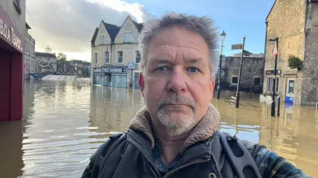 Jon Tilbury standing in front of a flooded Bradford-on-Avon town centre