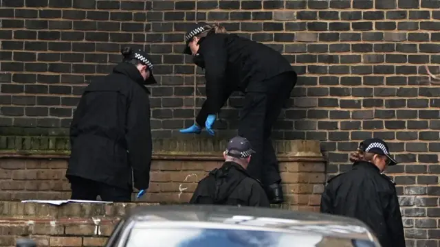 Two police officers climb a wall as others look on