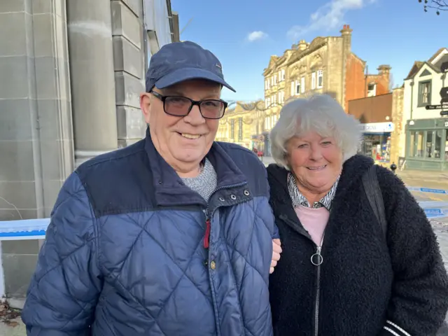 Ian and Sue Simpkins stand with their arms linked on Chippenham High Street