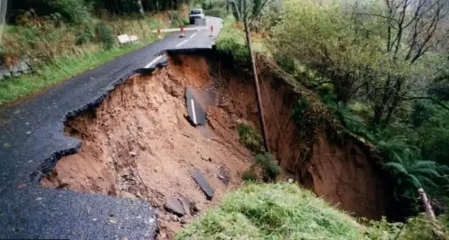 A landslide is seen in Northern Ireland. A large portion of the road is seen taken out with mud on the side.