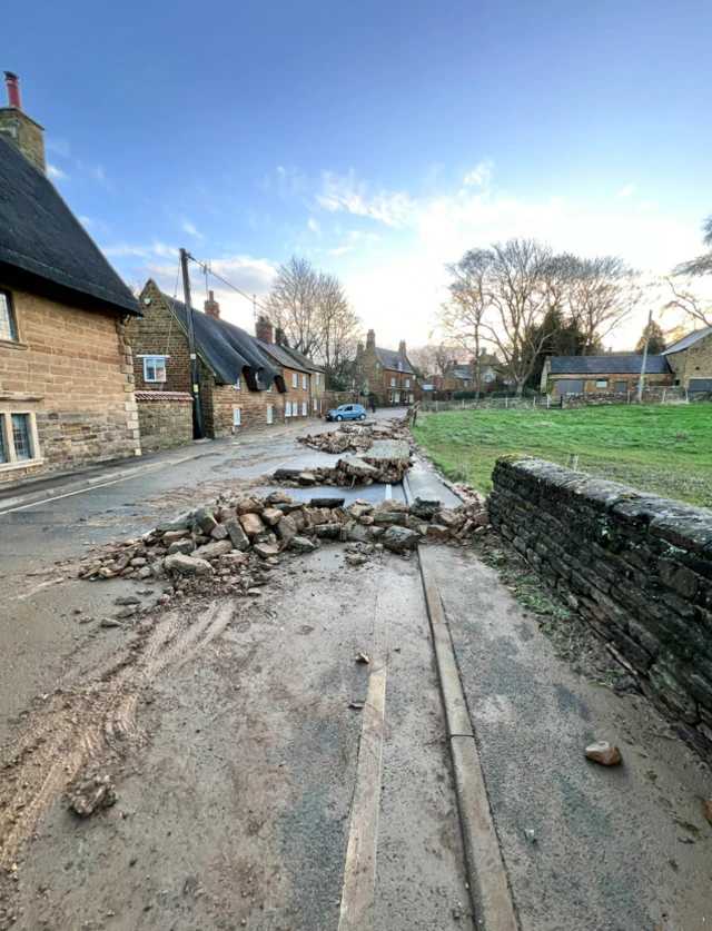 Big chunks of stone have fallen onto a road. The wall, which was opposite some houses, is missing a section.