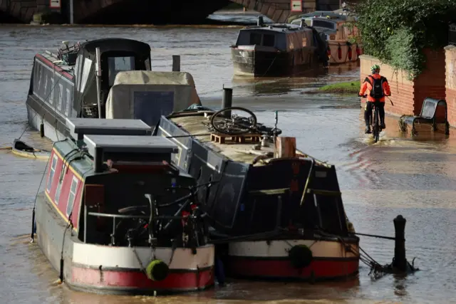 A cyclist wearing a orange hi-vis jacket while cycling through floodwater