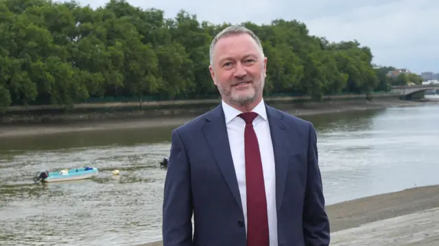 Environment Secretary Steve Reed, in a blue suit and red tie, standing by a river