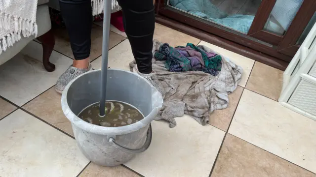 Dirty water in a bucket and wet towels on the floor of a home which was flooded