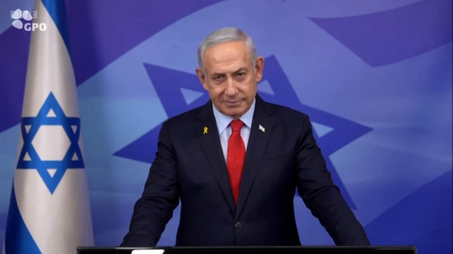 Netanyahu speaks at a lectern behind a blue background decorated with the star of david