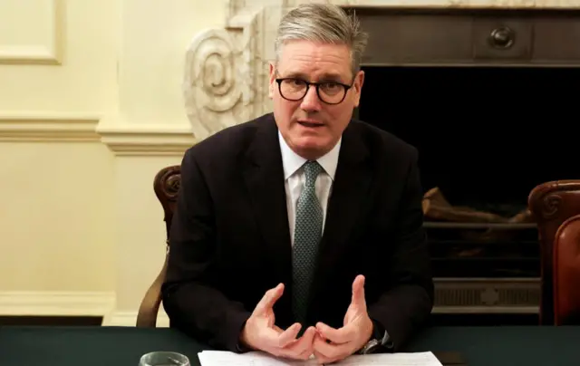 Starmer sits at a table, a folder of notes in front of him, speaking