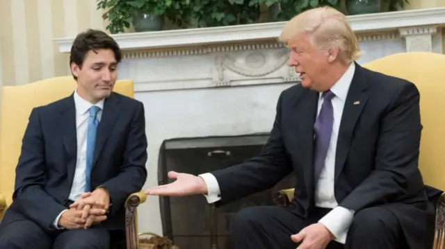 Justin Trudeau sits in a yellow chair. To his right, Donald Trump sits and holds out his hand