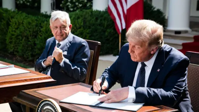 Trump sits outside, in front of the White House, with his pen to a document, with the then Mexican president sitting at a desk next to his