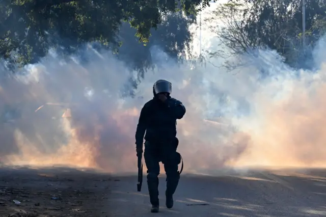 A policeman walks amid tear gas as supporters of Pakistan Tehreek-e-Insaf (PTI) party protest to demand the release of former prime minister Imran Khan, in Islamabad on November 26, 2024.