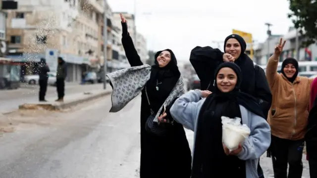 A group of women in Tyre, Lebanon, with smiles on their faces, one making a peace sign with fingers as another throws confetti-like substance into the air