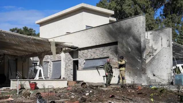 A soldier and an emergency responder stand in front of a building that is damaged and marked with burns on one side