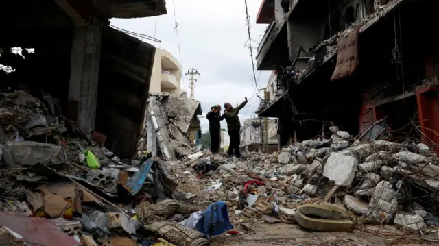 Milan Fakih, 40, father of Hashim Fakih, 10, and Fatima Fakih, 11, take a selfie together in front of their destroyed house,