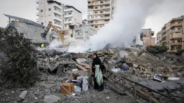 A woman looks for her belongings as she stands amidst the debris of a destroyed building