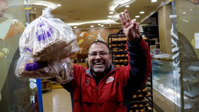 A man flashes the peace sign outside of a bakery