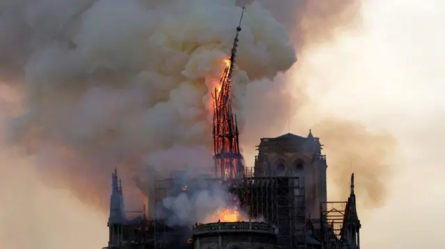 The blazing spire of Notre-Dame, engulfed in smoke as it breaks in half