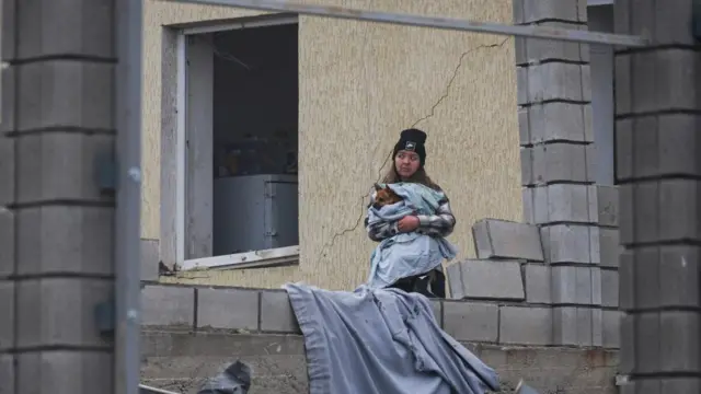 A resident holds a dog next to her house damaged by a Russian missile strike, amid Russia's attack on Ukraine, on the outskirts of Odesa,