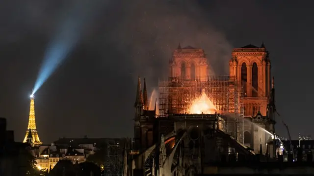 The last embers of the fire, now contained to the heart of the cathedral, burn at night with the Eiffel Tower visible in the background