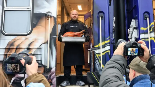 A man stands at the train door holding a turkey