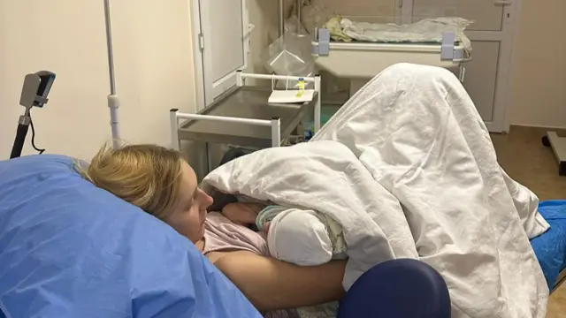 A mother rests in a hospital bed, cradling her child in her arms