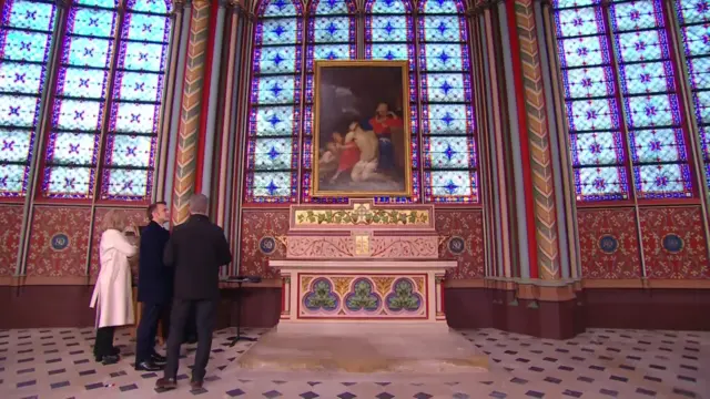 Macron is standing in front of colourful murals as he is being told the restoration process