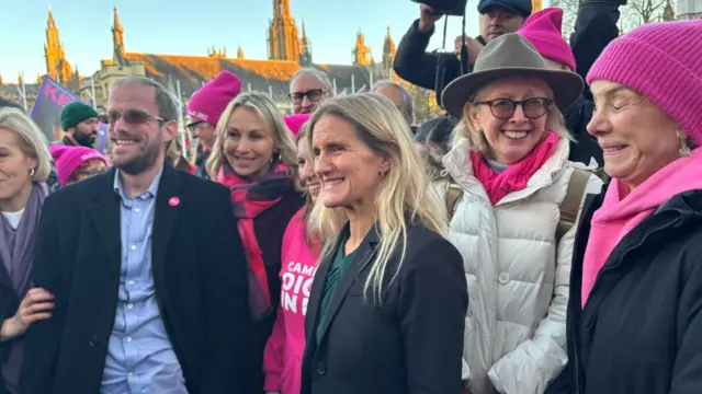 Kim Leadbeater stands with supporters dressed in pink in front of Parliament.