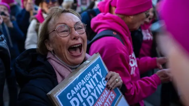 Woman looks ecstatic holding Campaign for Dignity in Dying placard among crowd of demonstrators wearing bright pink