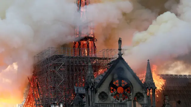 Notre-Dame in flames with smoke surrounding a spire and some scaffolding.