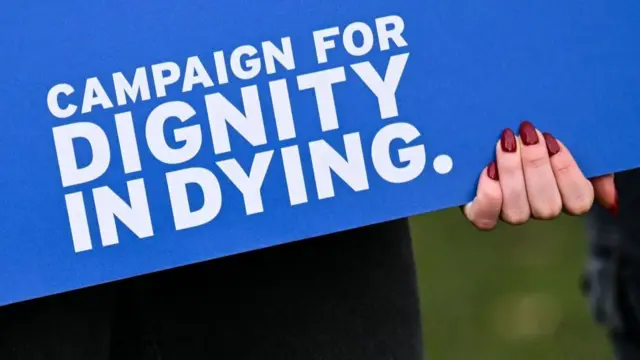 A woman holding a sign reading "campaign for dignity in dying"