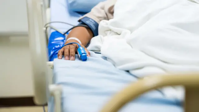 A male patient sleeps on the bed. A heart rate monitor is on his finger.