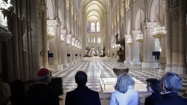 A group of people, including Emmanuel Macron, stand in the centre of the brightly-lit Notre-Dame Cathedral. There are arches and columns and high windows