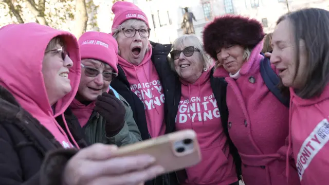 Six women wearing pink campaign clothes, look happy and relieved at the news.