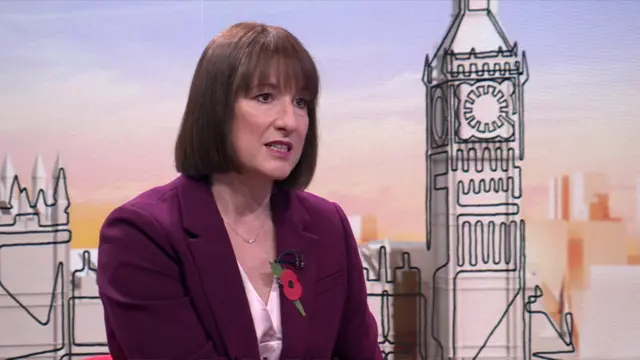 Rachel Reeves in plum suit jacket and white blouse sitting down on chair during interview