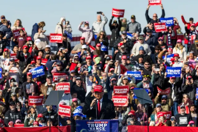 Trump addresses a crowd of supporters - many stood behind him are holding up signs saying "Trump will fix it" and "Dream big, again!"