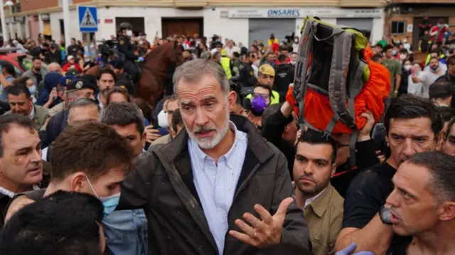 King Felipe in barbour jacket and striped shirt addresses angry crowd surrounding him in Valencia