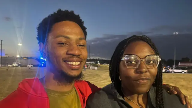 A man in a red hoodie and woman with glasses stand together outdoors