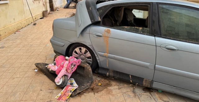 Image of a damaged car with children's bike next to it, covered in mud in Valencia after floods