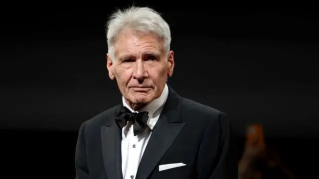 Harrison Ford, wearing a black tuxedo and bow tie over a white shirt, pauses for photos at the 76th annual Cannes Film Festival